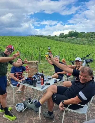 Fietsers proosten met bier aan een tafel voor een Toscaanse wijngaard
