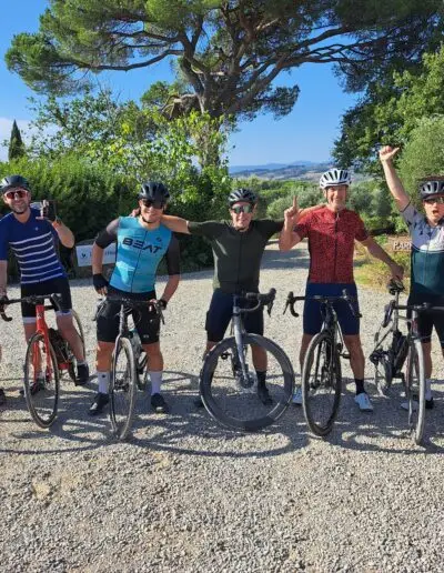 Vijf fietsers poseren juichend met hun fietsen op een grindoprit