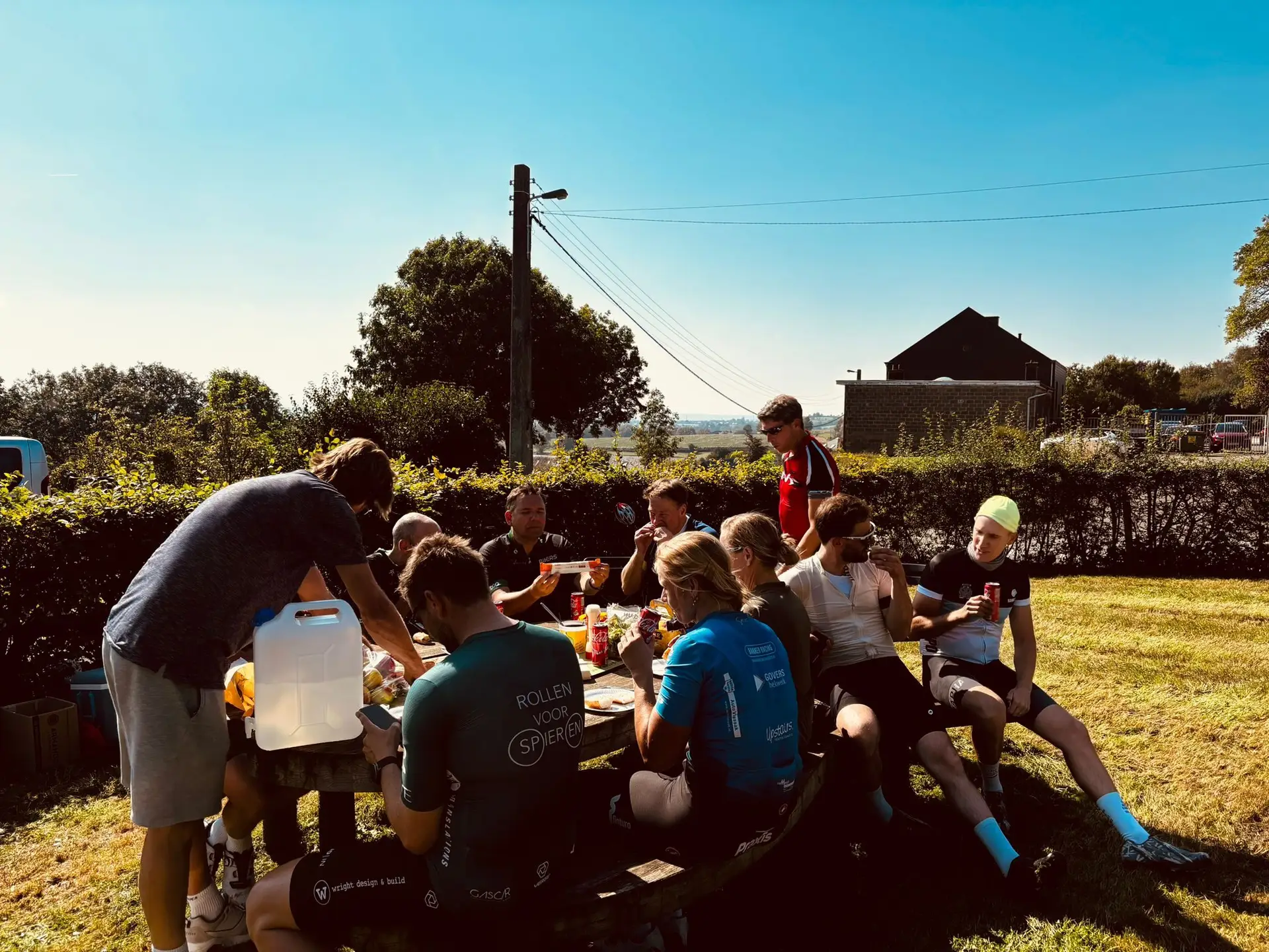 Fietsers aan een picknicktafel met drankjes in een zonnige tuin